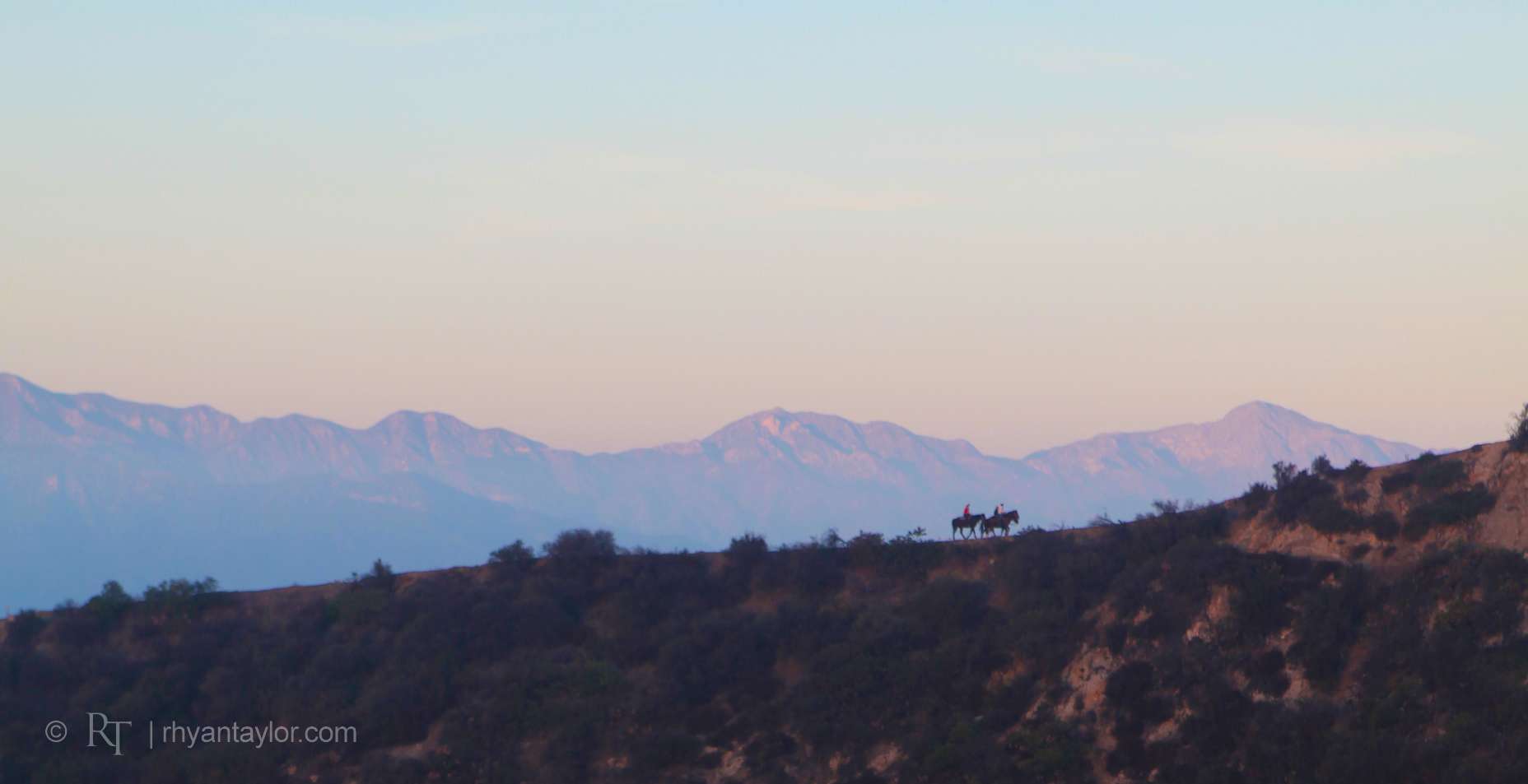Horseback riders on ridge against mountain backdrop